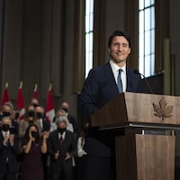 Le premier ministre Justin Trudeau debout devant un pupitre avec en arrière plan les membres de son nouveau gouvernement