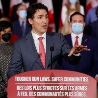 Justin Trudeau parle à des représentants des médias devant des députés libéraux assis derrière lui.