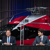 François Legault et Justin Trudeau sont assis à la table de presse devant un gros hélicoptère rouge.