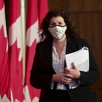 Karen Hogan marche en portant un masque et en tenant des documents dans ses mains.