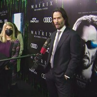 L'acteur répond aux question d'un journaliste avec une perche devant l'affiche du dernier film de la saga « La Matrice ».