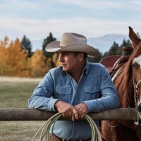 Kevin Costner, appuyé sur une clôture, en compagnie d'un cheval. 