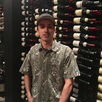 Un homme à casquette posant devant des étagères de bouteilles de vins.