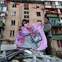 Deux hommes évacuent les débris d'une fenêtre devant leur immeuble.