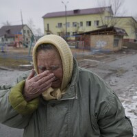 Une femme porte la main à son visage et pleure dans une rue jonchée de débris.
