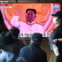 Des personnes portant un masque interagissent devant une télévision qui présente Kim Jong-un. 