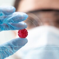 Une femme masquée et gantée tient une représentation du coronavirus entre les doigts.
