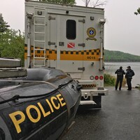 Un camion de la Sûreté du Québec transportant derrière lui un bateau pneumatique avec l'inscription Police est stationné au bord d'un lac. 