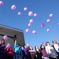 Des ballons violets remplis d'hélium s'élèvent vers le ciel alors que des dizaines de personnes les laissent aller.