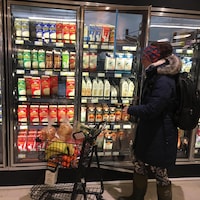 Une femme poussant un petit chariot d'épicerie passe devant des réfrigérateurs contenant du lait dans un supermarché.