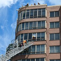 Des pompiers sur une échelle secourent des personnes coincées à l'extérieur d'un immeuble de grande hauteur.