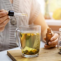 Une femme met de l'huile de cannabis à l'aide d'une pipette dans un thé.
