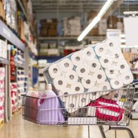 Un panier rempli de produits, notamment de rouleaux de papier toilette, dans un supermarché.