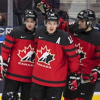 Trois joueurs du Canada en uniforme rouge et noir après avoir célébré un but.