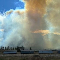 Le feu de forêt Nohomin Creek brûle à bonne distance, derrière trois maisons. 