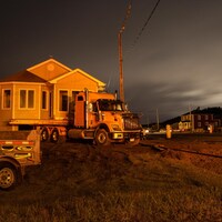 Une maison déposée sur un camion-remorque doit être déplacée de l'autre côté d'une route en pleine nuit.