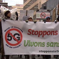Une bannière sur laquelle est inscrit: Stoppons la 5G  est tenue par plusieurs manifestants.
