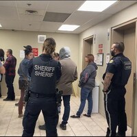 Des policiers et des résidents dans un couloir devant des ascenseurs.