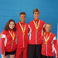 Quatre jeunes athlètes posent avec leur médaille, sur un podium.