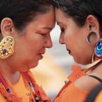 Deux femmes autochtones se serrent, les larmes aux yeux.