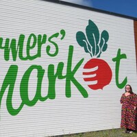 Une femme se tient debout près du mur extérieur sur lequel le logo du marché est peint.