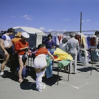 Clients devant un kiosque de vêtements au marché aux puces Saint-Hippolyte.