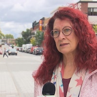 Une femme qui porte des lunettes et aux cheveux rouges en entrevue à Radio-Canada.