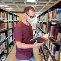 Un homme portant un masque feuillette un livre dans une bibliothèque.