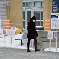 Une personne qui porte un masque marche sur un trottoir devant l'hôpital de Rimouski. 