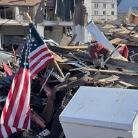 Maison complètement détruite, avec drapeau américain et peluches sur les décombres
