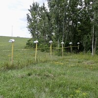 Des poteaux sur lesquels repose une petite boîte blanche et reliés entre eux par une corde.