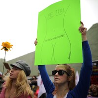 Dans une manifestation, une femme lève une pancarte jaune fluo qui dit aux agresseurs sexuels « Vous savez qui vous êtes ».