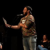 L'homme sourit debout devant un micro, une feuille à la main.