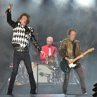 Un chanteur est accompagné d'un batteur et d'un guitariste sur scène.