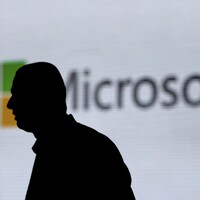 La silhouette d'un homme se dessine sur un écran où est projeté le logo de Microsoft. 