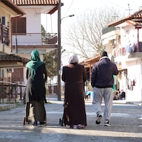 Un homme et deux femmes voilées marchent dans la rue.