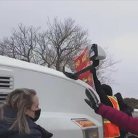 Un homme avec un dossard de construction brandit une pancarte sur laquelle il est inscrit : "SVP, Arrêtez." Il est complètement collé sur le camion qui avance en sa direction.