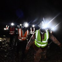 Une demi-dizaine de personnes avec des lampes frontales avancent dans une galerie de la mine. (16 avril 2022)