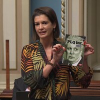 Geneviève Guilbault, debout à l'Assemblée, tient un livre avec Jean Charest sur la couverture.