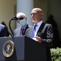 Il est devant un lutrin sur lequel se trouve un microphone.