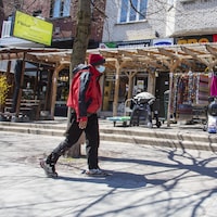 Un passant, qui porte un masque, marche dans une rue commercial de Montréal.