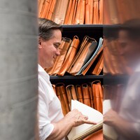 Le musicothécaire de l'OSM, Michel Léonard, feuillette une partition alors que son visage est reflété sur une étagère en métal.
