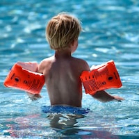 Un jeune enfant dans l'eau d'une piscine avec des flotteurs aux bras.