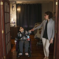 Une mère, debout, et son fils, en fauteuil roulant, se regardent l'air songeur.