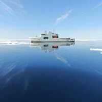 Le NCSM Harry DeWolf navigant sur un océan ou flotte quelques plaques de glace.