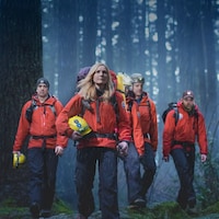 Cinq membres de North Shore Rescue marchent en forêt. 