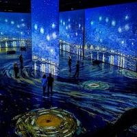 Des gens dans une salle où des toiles de Vincent Van Gogh sont projetées sur les murs et le plancher.