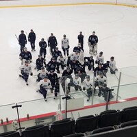 Une trentaine de jeunes joueurs de hockey écoutent leur entraîneur sur la patinoire.