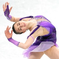 Une patineuse artistique place ses mains au-dessus de sa tête en faisant une figure.