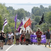 Des Mohawks de Kanesatake marchent dans une rue en brandissant des drapeaux. 
